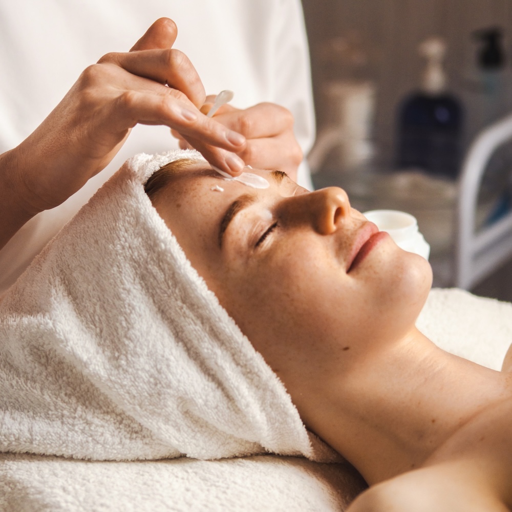 woman smiling and relaxing while having a facial treatment